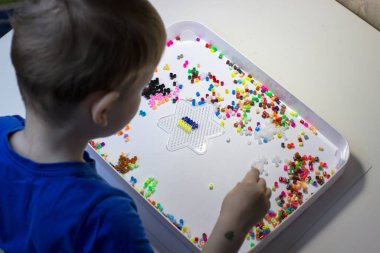 Bir çocuk termo mozaik çalıyor. Beyaz masada oynayan bir çocuk.