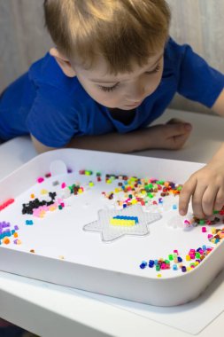 Bir çocuk termo mozaik çalıyor. Beyaz masada oynayan bir çocuk.
