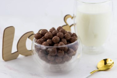 Çikolata topları şeklinde atıştırmalıklar. Kahvaltılık bir kase, bir bardak süt ve beyaz mermer arka planda yazılan aşk.