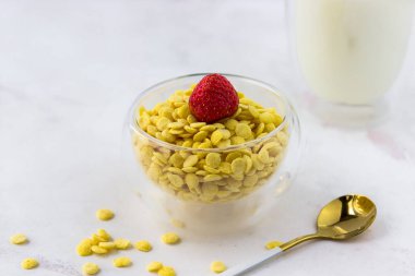 Beyaz mermer bir masada bir kase kahvaltı gevreği ve bir bardak süt. Çilekli mısır gevreği.