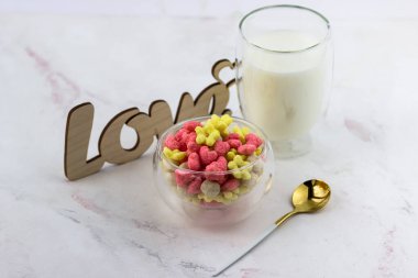 Bir kase kahvaltı gevreği, bir bardak süt ve beyaz bir masaya yazılmış ahşap bir aşk yazısı. Romantik kahvaltı.