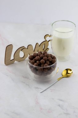 Çikolata topları şeklinde atıştırmalıklar. Kahvaltılık bir kase, bir bardak süt ve beyaz mermer arka planda yazılan aşk.