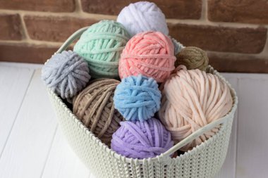 Pastel renklerde pelüş ipliklerle dolu bir sepet. Örgü sepeti beyaz bir masada.
