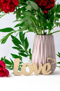 Üzerinde kırmızı şakayık demeti olan bir kartpostal ve beyaz arka planda ahşap bir yazı var.