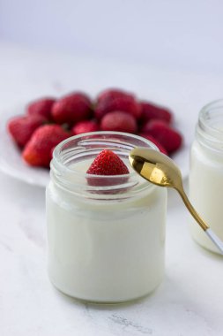 Ev yapımı yoğurt. Beyaz bir masada kavanozlar dolusu yoğurt ve çilek. Uygun beslenme