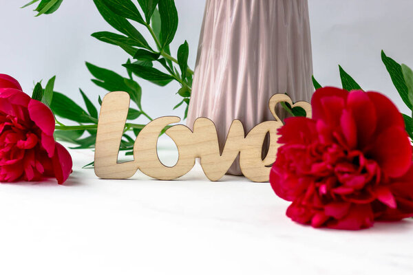 Wooden inscription love on a background of peonies on a white background. Postcard with text space