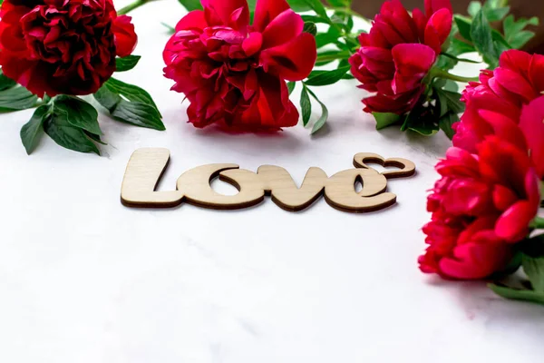 Wooden inscription love on a white background. Postcard with peonies on a white background. Space for text