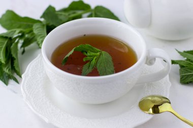 Tea with mint in a white cup and a white teapot on a white marble background. Morning tea