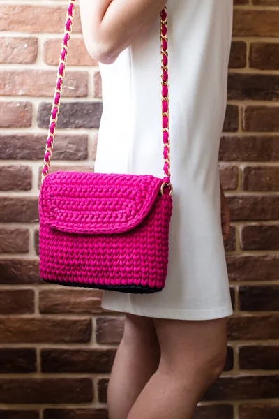 Knitted bag on a girl in a white dress against a brick wall