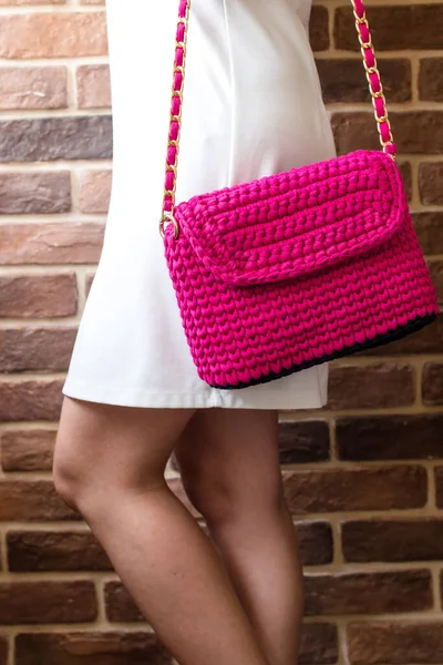 Knitted bag on a girl in a white dress against a brick wall