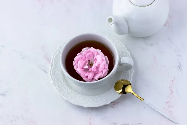 Tea with tea rose in a white cup on a white marble table.