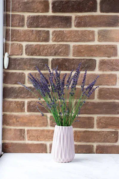 A bouquet of fresh lavender in a vase by the window. Flowers on the background of a brick wall