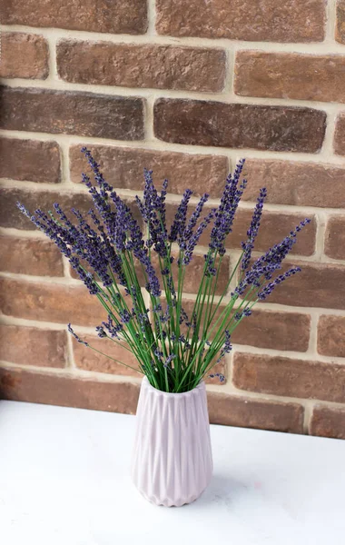 A bouquet of fresh lavender in a vase by the window. Flowers on the background of a brick wall