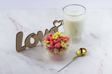 Bir kase kahvaltı gevreği, bir bardak süt ve beyaz bir masaya yazılmış ahşap bir aşk yazısı. Romantik kahvaltı.