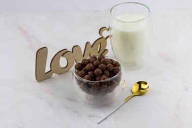 Çikolata topları şeklinde atıştırmalıklar. Kahvaltılık bir kase, bir bardak süt ve beyaz mermer arka planda yazılan aşk.