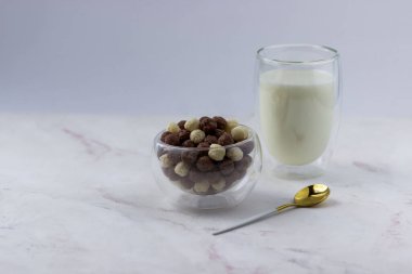 Beyaz arka planda vanilyalı ve çikolata toplu bir kase. Atıştırmalık ve bir bardak süt - hızlı kahvaltı