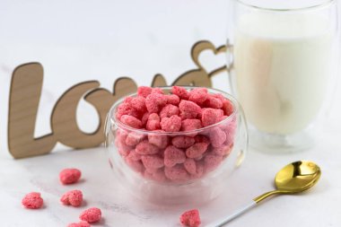 Bir kase kahvaltı gevreği, bir bardak süt ve beyaz bir masaya yazılmış ahşap bir aşk yazısı. Romantik kahvaltı.