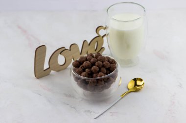 Çikolata topları şeklinde atıştırmalıklar. Kahvaltılık bir kase, bir bardak süt ve beyaz mermer arka planda yazılan aşk.