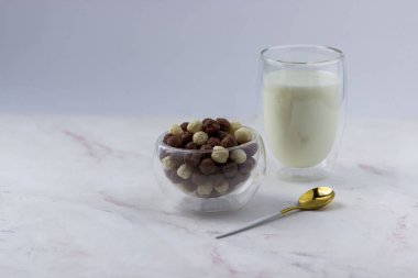 Beyaz arka planda vanilyalı ve çikolata toplu bir kase. Atıştırmalık ve bir bardak süt - hızlı kahvaltı