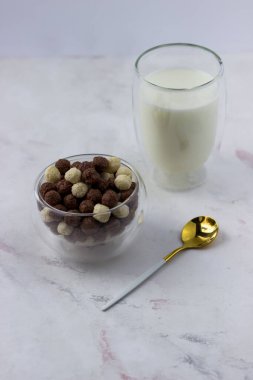 Beyaz arka planda vanilyalı ve çikolata toplu bir kase. Atıştırmalık ve bir bardak süt - hızlı kahvaltı