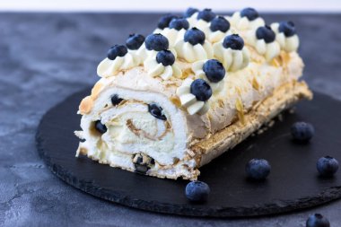 Koyu arkaplanda kremalı pasta rulosu. Yaban mersinli tatlı