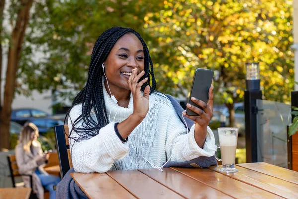 Güzel bir Afro-Amerikalı kız ve arka planda bir sarışın, bir kafede dinleniyorlar ve cep telefonlarıyla sosyal ağlardan konuşuyorlar. Boş zaman ve şehir yaşam tarzı.