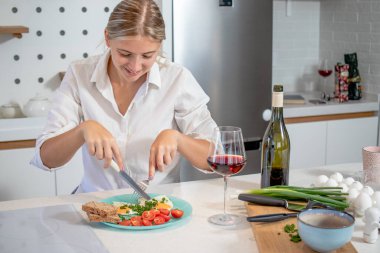 Modern bir dairede tek başına yemek yiyen güzel bir genç kadın. Çeri domatesli yumurta ve serpilmiş soğan. Kahvaltı mı, akşam yemeği mi?.