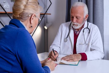 Deneyimli bir doktor, yaşlı bayan hastasıyla özel tıbbi dosyasını tartışıyor. Orta yaşlı bir kadın doktorunu kontrol ediyor ve sağlık ve sağlık sigortası hakkında danışmanlık yapıyor..