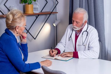 Deneyimli bir doktor, kıdemli bir kadın hasta için reçete yazıyor. Orta yaşlı bir kadın doktorunu kontrol ediyor ve sağlık ve sağlık sigortası hakkında danışmanlık yapıyor..