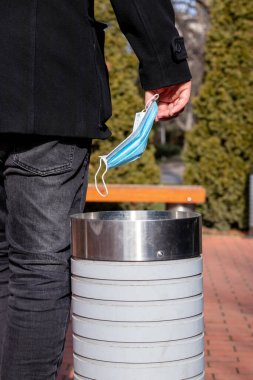 Sokaktaki çöp kutusuna yüz maskesi atan bir adamın eli. Coronavirus veya Covid-19 tıbbi atık konsepti. Salgın krizinin sonu.