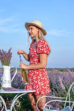 Güzel genç bir kadın güneşli bir yaz öğleden sonrasında lavanta tarlasında bir şişe şarap açar..