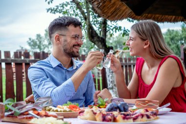 Genç ve mutlu romantik çift, güzel bir açık hava restoranında, dar bir gözlüklü brendi ile kadeh kaldırıyor..
