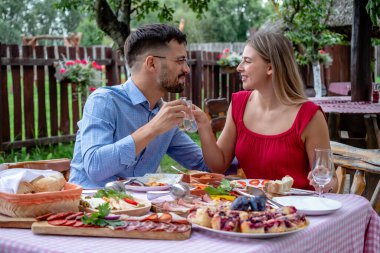 Genç ve mutlu romantik çift, güzel bir açık hava restoranında, dar bir gözlüklü brendi ile kadeh kaldırıyor..