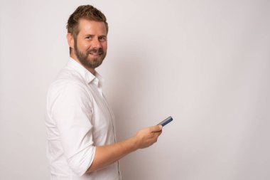 Profil tarafı fotoğrafı, pozitif neşeli bir adamın beyaz arka planda cep telefonunu tutarken çekilmiş..