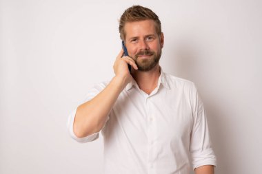 Beyaz arka planda cep telefonuyla konuşan yakışıklı genç adam.