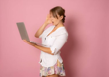 Pembe arka planda dizüstü bilgisayarı olan mutlu ve şaşırmış genç bir kadının portresi. Metin için boşluk.