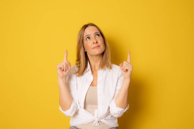 Sarı arkaplanı işaret eden güzel genç bir kadının portresi.