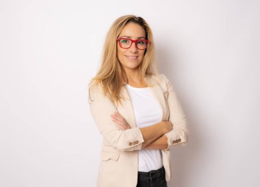 Beyaz bir arka plana dayanır katlanmış ellerle gülümseyen iş kadını.