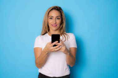 Mavi arka planda izole edilmiş cep telefonu kullanan güzel bir kadın..