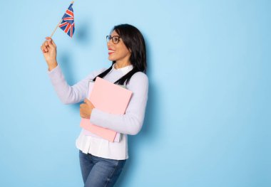 Elinde kitaplarla gülümseyen kadın. Mavi arka planda İngiliz bayrağı taşıyan okul öğretmeninin izole edilmiş portresi..