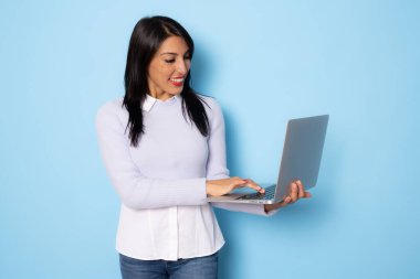 Mavi arka planda dizüstü bilgisayar kullanarak izole edilmiş neşeli genç bir kadın görüntüsü.