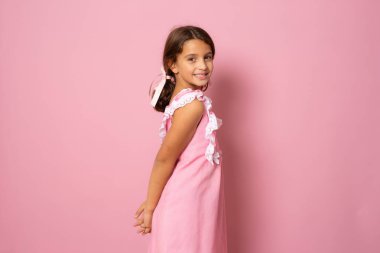 Pembe elbiseli güzel bir kızın portresi pembe arka planda izole edilmiş poz veriyor..