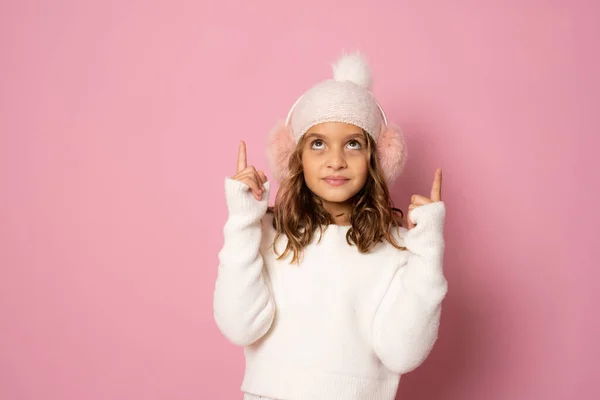 Cute Girl Noszenie Stylowe Nauszniki Wskazujące Palce Górę Różowym Tle — Zdjęcie stockowe