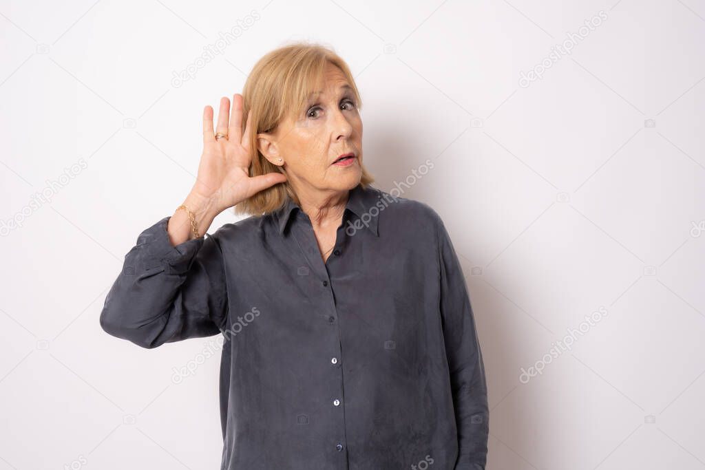 Portrait of cheerful old woman in blue shirt making listening gesture, isolated on white background