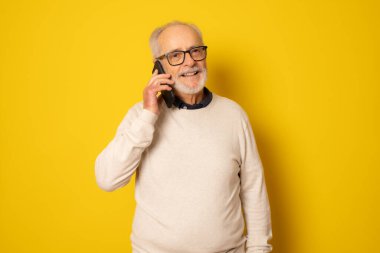 Sarı arka planda izole akıllı telefon kullanan mutlu kıdemli adam..