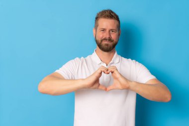 Mavi arka planda elleri soyutlanmış kalp figürü yapan genç yakışıklı adam..