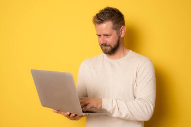 Sarı arka planda izole edilmiş dizüstü bilgisayar kullanan yakışıklı bir genç..