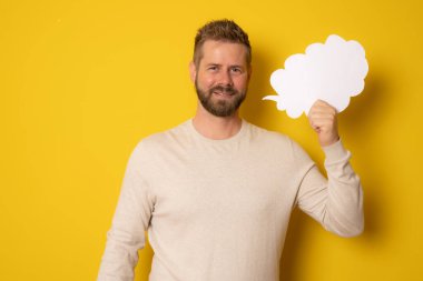 Sarı arka planda izole genç beyaz adam boş bir konuşma balonu tutuyor.