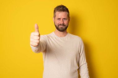 Başparmağı havada genç hippi, sarı arka planda izole edilmiş..