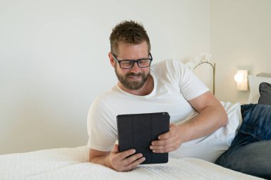 Elinde tabletle yatan gülümseyen genç adam.